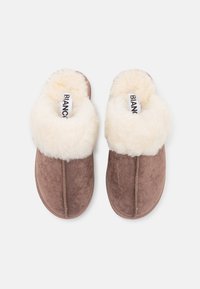 Chaussons en daim marron avec un revers en fourrure crème moelleuse, présentant une couture au centre et une étiquette de marque à l'intérieur.