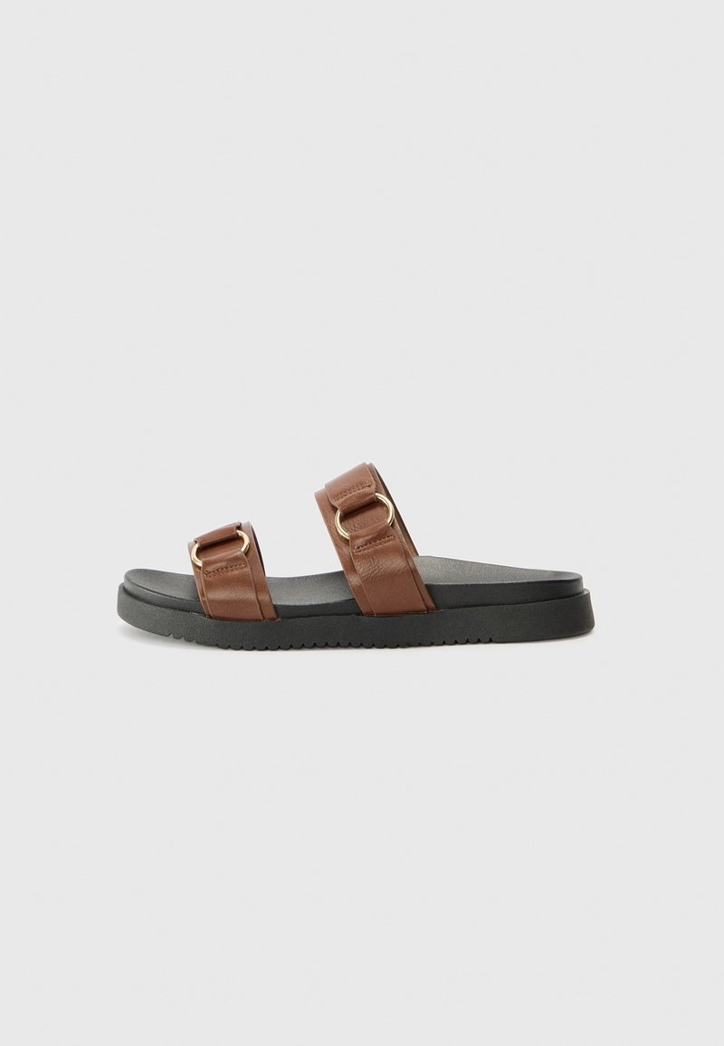 Mules en cuir marron avec deux brides ajustables dotées de quincaillerie dorée. Semelle en caoutchouc noir avec une surface texturée pour une meilleure adhérence.