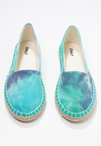 Espadrilles en toile turquoise avec un motif tie-dye, semelles en corde de jute et détails cousus le long du bord.