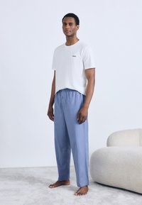 Hvit bomulls-T-skjorte med "BOSS"-logo, kombinert med lyseblå snorbukser i et mykt stoff, brukt av en stående modell.