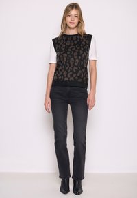 Schwarz leopardgemusterter Strickpullover mit kurzen weißen Ärmeln, kombiniert mit dunklen Jeans und schwarzen Knöchelstiefeln. Glatte Textur, taillierte Passform.