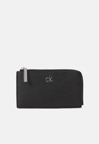 Svart skinnlommebok med glidelås, med sølvlogo og glatt tekstur, rektangulær form og minimalistisk design.