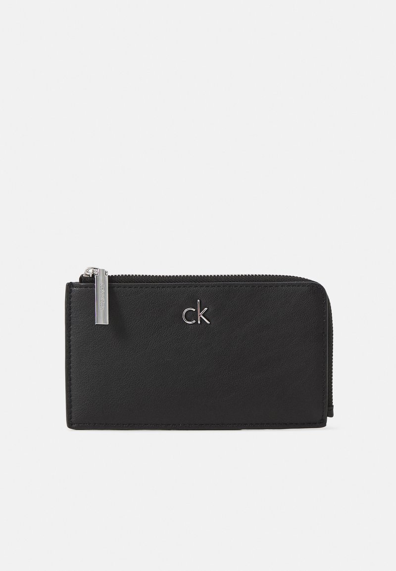 Svart skinnlommebok med glidelås, med sølvlogo og glatt tekstur, rektangulær form og minimalistisk design.