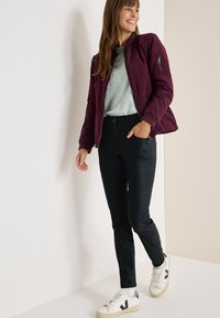 Bordeauxjakke med lynlås foran, grå top, sort slankebukser og hvide sneakers med sorte accenter. Glat stof og afslappet pasform.