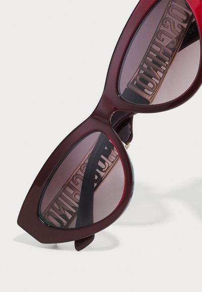 Burgundy kattögon-solglasögon med tonade linser, med en djärv design och prägling av logotypen på skalmen. Glansigt plastmaterial.
