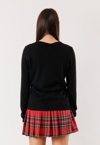 Maglione nero con maniche lunghe e collo tondo, abbinato a una gonna plissettata a scacchi rossa con accenti neri e gialli.