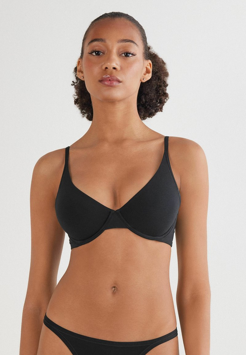 Černá podprsenka s kosticemi vyrobená z hladké tkaniny, s nastavitelnými ramínky a klasickým V-střihem, minimalistickým šitím a bez ozdob.