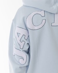 Šviesiai mėlynas džemperis su didelėmis tekstūruotomis baltomis raidėmis kairiajame rankovėje. Minkšta, medvilninė medžiaga su laisvu siluetu.