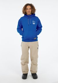 Blauwe hoodie met een voorzak, met een logo. Beige broek met zijzakken, gecombineerd met zwarte laarzen. Eenvoudig ontwerp.