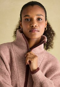 Helles Rosa, geripptes Zip-up-Sweater mit hohem Kragen und bordeauxfarbenen Akzenten. Verfügt über ein strukturiertes Material und enge Bündchen.