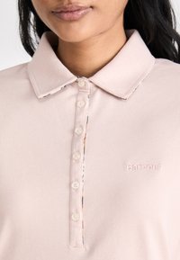 Camisa polo rosa claro feita de tecido texturizado. Apresenta um colarinho clássico, cinco botões e o logótipo bordado 'Barbour' do lado esquerdo.
