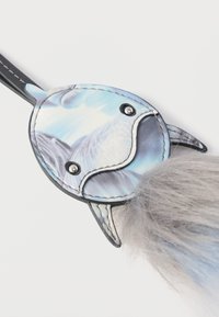 Μπρελόκ από ψεύτικη γούνα σε σχήμα ψαριού· μπλε και λευκό σχέδιο σε λεία επιφάνεια με μαύρο περίγραμμα, με χνουδωτή γκρι ουρά και ασημένιες λεπτομέρειες.