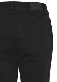 Mustade teksade lähivõte, kus on näha tagataskud, vööaugud ja õmblused kangal.