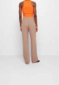 En orange ärmlös topp i tank-stil matchad med högmidjade, vida beige byxor. Slätt tyg med en avslappnad passform. Svart skor syns.