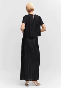 Schwarzes, plissiertes Zweiteiler-Outfit mit einem kurzen Oberteil und langem Rock. Verfügt über kurze Ärmel, ein Schlüsselaugen-Detail am Rücken und eine glatte Textur.