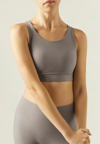 Grå sportsbh lavet af glat stof med en scoop halsudskæring. Den har et cropped design, minimale sømme og en tætsiddende pasform.