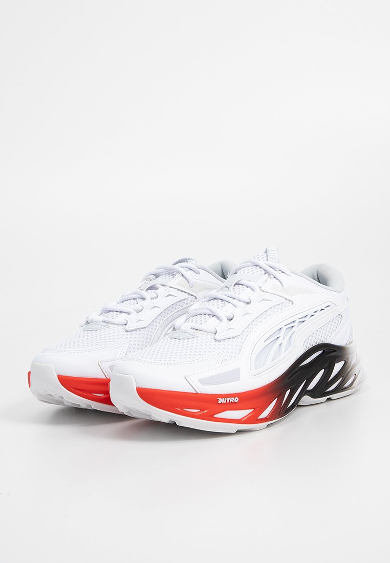 Baskets de sport blanches avec un dessus en maille, des accents noirs et rouges, et un design de semelle courbée distinctif. Comprend des lacets et un col rembourré.