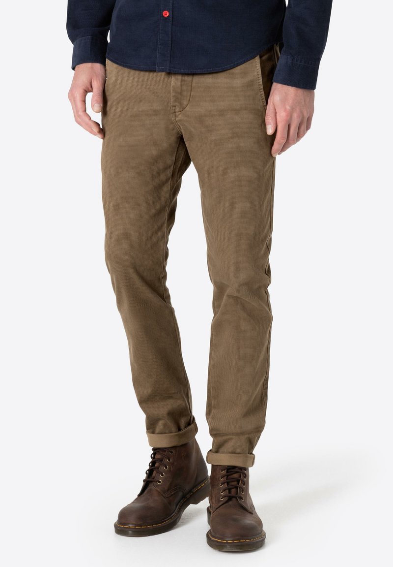 Brown corduroy trousers with a straight fit, featuring a subtle ribbed texture. Worn with dark lace-up leather boots.