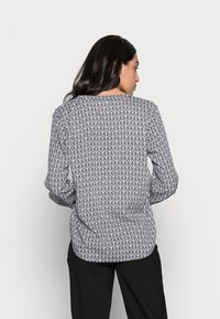 Blusa a maniche lunghe con un motivo geometrico di foglie in bianco e nero, con scollatura rotonda e orlo posteriore leggermente arricciato.