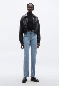 Crna kožna kratka jakna, crni rolka, svijetloplave traperice s visokim strukom i crne cipele. Naglasak na prilagođenom dizajnu i čistim linijama.