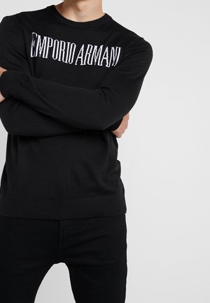 Schwarzer Strickpullover mit Rundhalsausschnitt und gerippten Bündchen, mit dem Logo "EMPORIO ARMANI" in kontrastierendem Weiß über der Brust.