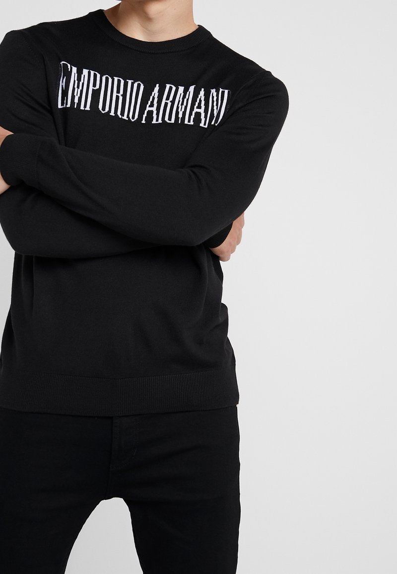 Svart stickad sweatshirt med rund hals och ribbade ärmslut, med "EMPORIO ARMANI"-logotyp i kontrasterande vitt över bröstet.