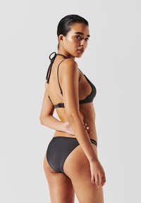Svart bikinitopp med triangeldesign och snörning samt lågmidjade underdelar. Materialet har en subtil lyster. Enkelt mönster med minimal täckning.