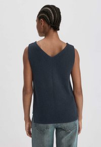 Navyblauw gebreid mouwloos topje met een V-hals, met een geweven patroon en een losse pasvorm, gecombineerd met lichtblauwe denim jeans.