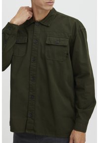 Giacca camicia verde oliva in cotone, con chiusura a bottoni, due tasche sul petto e maniche lunghe con polsini abbottonati.