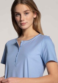 Lichtblauwe shirt met korte mouwen en een ronde halslijn, drie knoopsluiting en een gladde stofstructuur. Geen opvallende patronen of hardware.