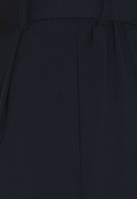 Mörkblått tyg med matt yta, med vertikala veck och synlig sömnad. Skräddarsydd design med en ren, strukturerad silhuett.