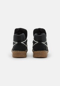 Zapatillas altas negras con tejido texturizado, cordones elásticos y suelas de goma con diseño moteado. La vista trasera muestra un cuello acolchado.