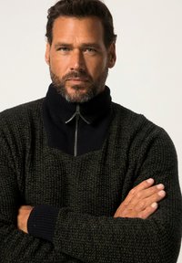 Maglione lavorato a maglia di colore verde scuro con motivo testurizzato. Presenta un alto colletto nero e chiusura con mezza zip. I polsini a coste offrono un contrasto.