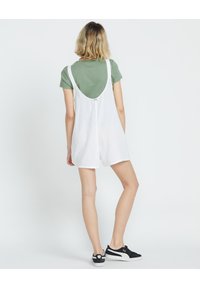 Abito lungo in lino bianco con scollatura a barco, indossato sopra una maglietta verde. Abbinato a sneakers bianche e nere.