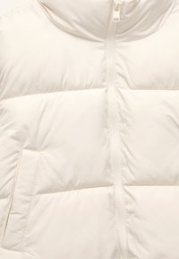 Bijela podstavljena jakna s visokim ovratnikom, patentnim zatvaračem, horizontalnim šavovima i diskretnim bočnim džepom. Glatki, lagani materijal.