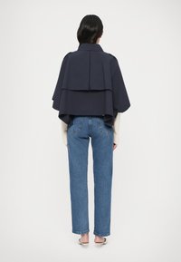 Jachetă în stil capă, de culoare bleumarin, cu design stratificat, strat interior contrastant și croială supradimensionată. Combinată cu blugi albastri cu talie înaltă și tocuri.