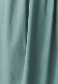 Mīksta, fakturēta gaiši zila auduma ar vieglām vertikālām krokām un redzamu austā rakstu tuvplānā.