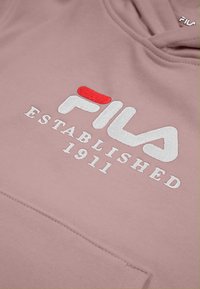 Sudadera rosa con logo "FILA" bordado en rojo y blanco, con el texto "ESTABLISHED 1911." Diseño sencillo y textura suave.