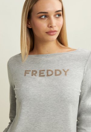 Sweatshirt gris à manches longues en tissu doux, avec "FREDDY" en écriture scintillante sur la poitrine et un col décontracté.