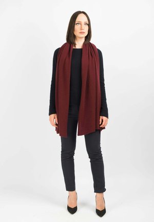 Sciarpa bordeaux in morbido tessuto, che si drappeggia in modo elegante. Abbinata a un maglione nero e pantaloni scuri aderenti, completata da decolletè nere.