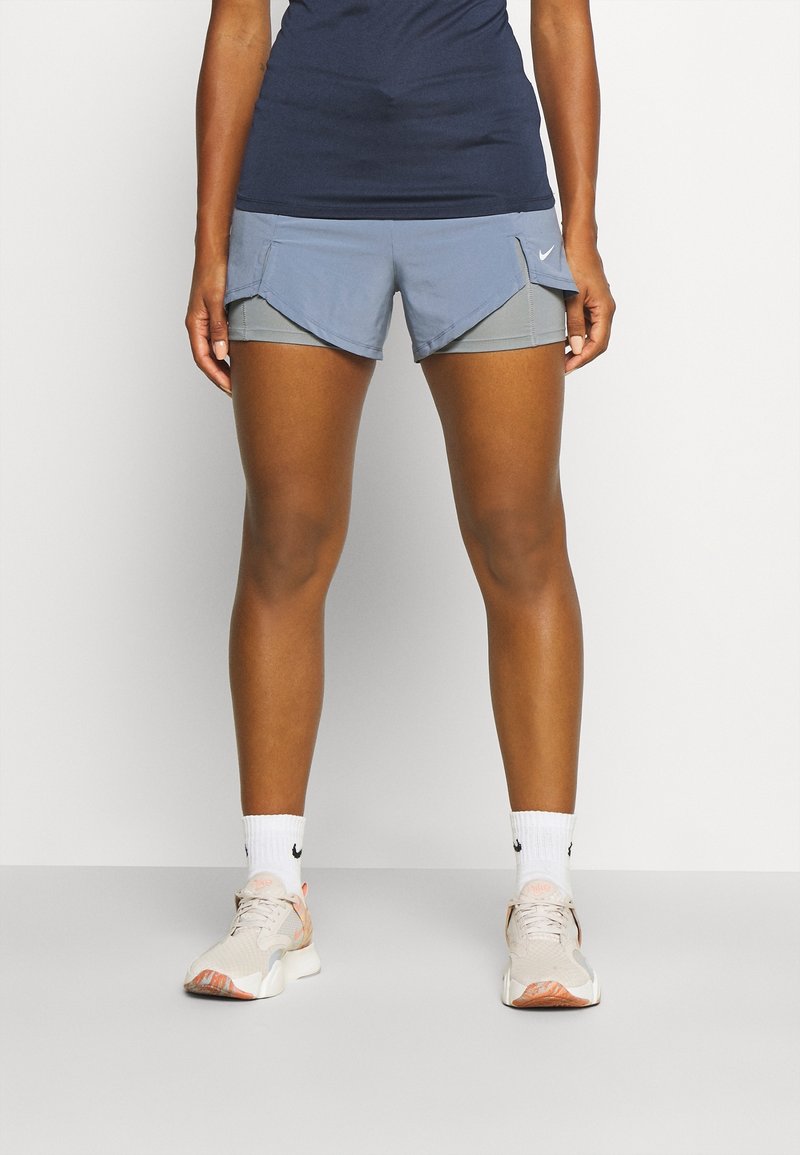 Pantalones cortos Nike en azul claro con diseño en capas, que cuentan con bolsillos y una textura suave. Llevados con calcetines blancos y zapatillas deportivas beige.