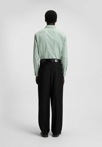 Light green long-sleeve shirt with buttoned cuffs paired with black loose-fitting trousers, viewed from the back. Smooth fabric texture.
