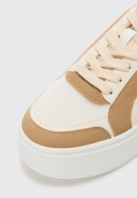 Baskets avec une semelle en caoutchouc blanc, un dessus en daim et en mesh beige, dotées de lacets et de coutures beige. Bout arrondi et accents texturés.