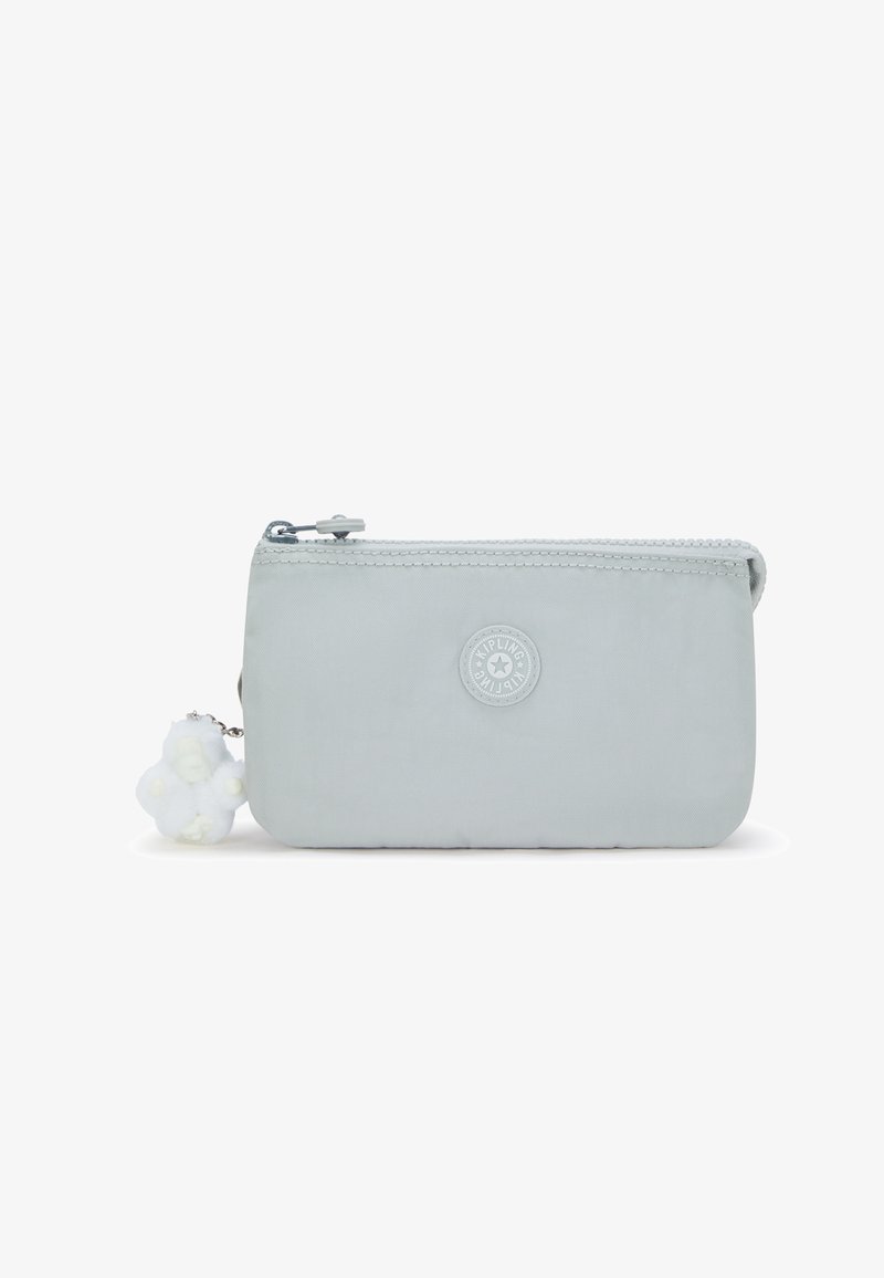 Trousse rectangulaire gris clair avec une fermeture éclair, ornée d'un patch logo rond et d'un petit porte-clés blanc pelucheux attaché à la fermeture éclair.