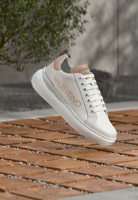 Weißer Ledersneaker mit rosa Akzenten, ausgestattet mit einer abgerundeten Zehenpartie, Schnürverschluss und einem eingeprägten "VALENTINO"-Logo an der Seite.