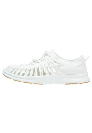 White open-weave sandal with closed heel, adjustable lace, and a flat sole with light brown tread, viewed from the side.