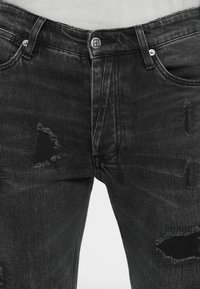 Sorte denimjeans med slitte lapper, med knappelukking og fem lommer. Materialet har en lett ru tekstur.