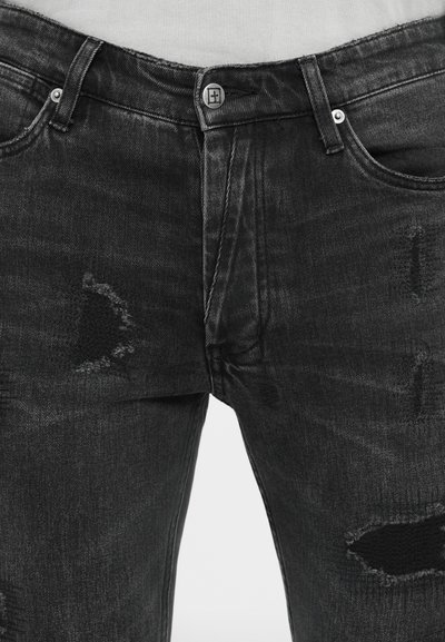 Jeans in denim nero con toppe strappate, dotati di chiusura a bottone e cinque tasche. Il materiale ha una texture leggermente ruvida.