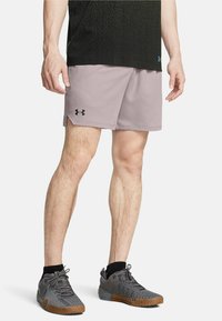 Vaaleanpunaiset urheilushortsit, joissa on musta Under Armour -logo, sivuleikkaukset, yhdistettynä harmaisiin lenkkareihin, joissa on teksturoitu päällinen ja ruskea pohja.