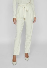 Kreemivärvi kõrge taljega volditud püksid, mis on varustatud seotud vöö ja kitsenevate jalgadega, koos terava ninaga beežide kontsadega. Sile, kerge kangas.